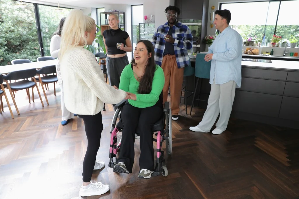 Disabled woman in wheelchair talking with support worker and friends at home