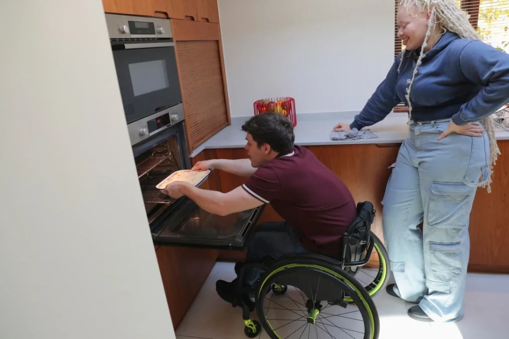 Disabled man putting lasagne in oven with friend