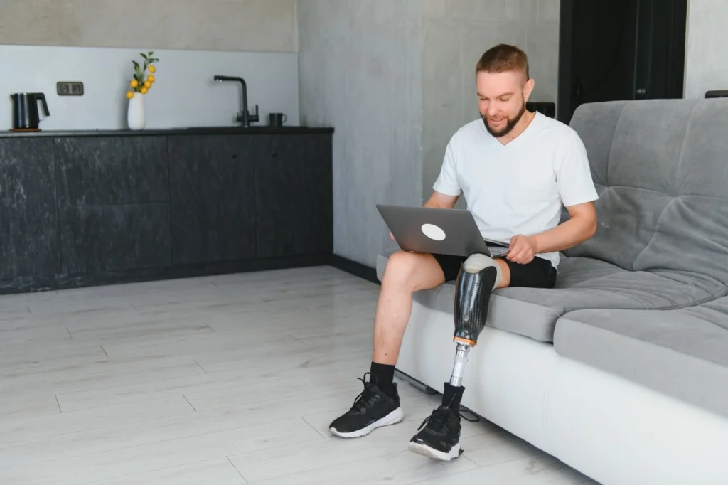 Disabled man with amputated leg sitting on couch with laptop